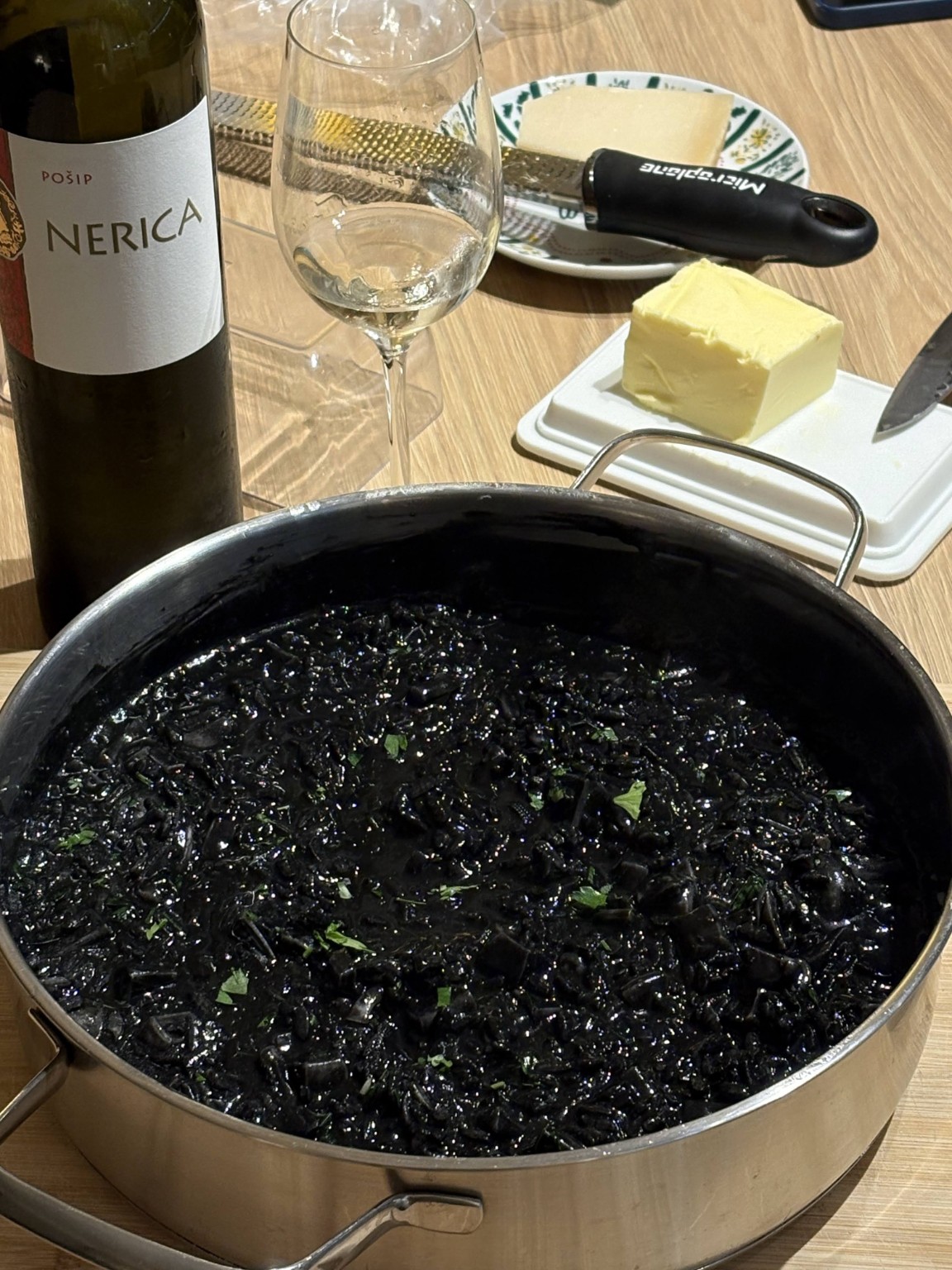Black cuttlefish risotto in a pan, topped with chopped parsley.