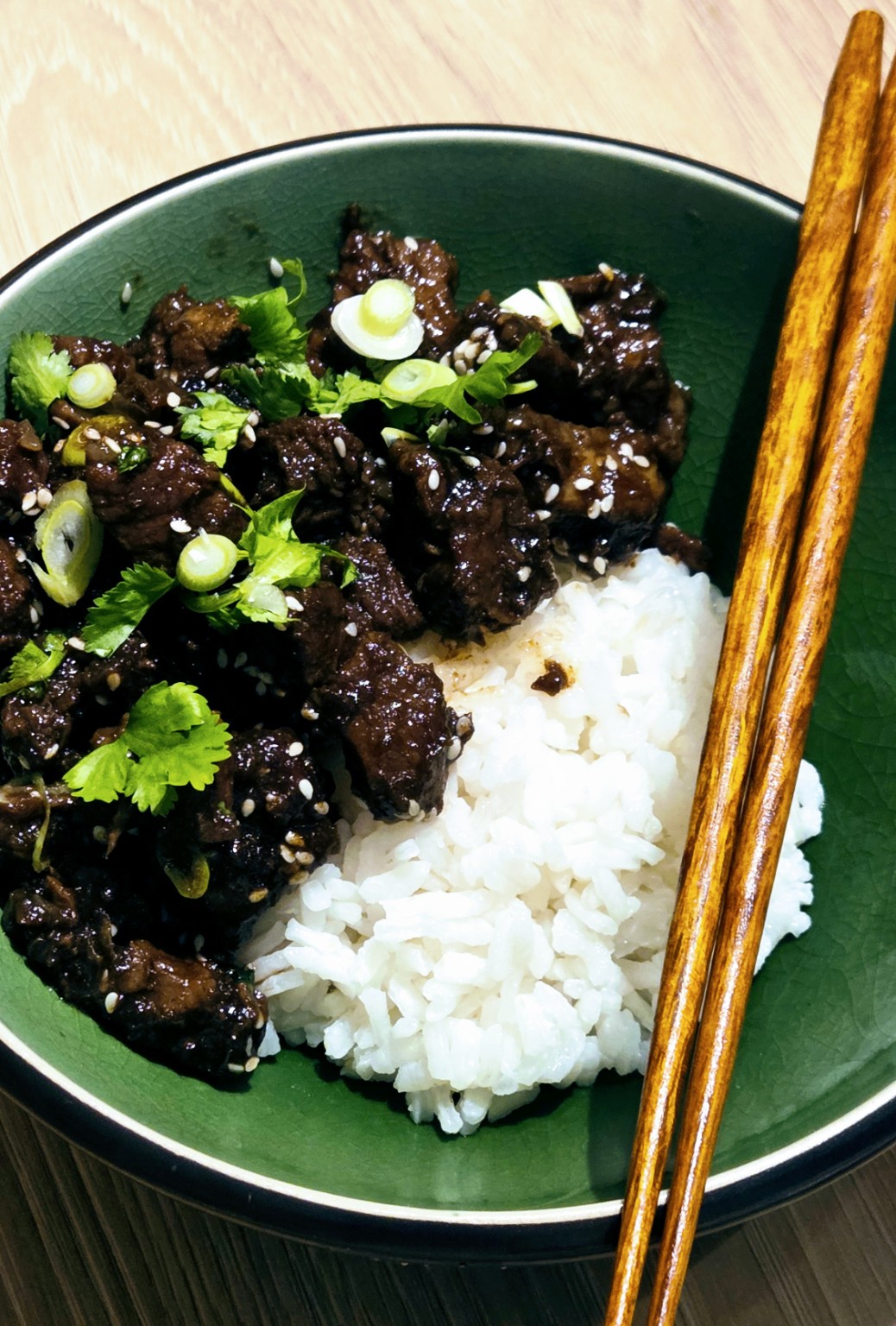 Vietnamese caramel pork over sticky rice in a green bowl, garnished with scallions, coriander and sesame seeds, with chopsticks.